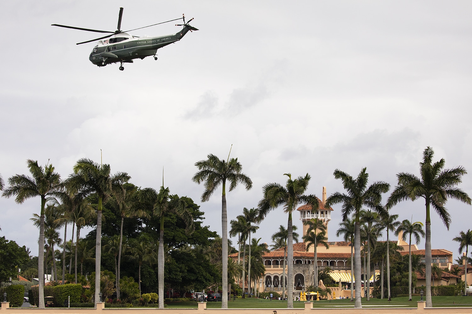 Marine One helicopter hovers over palm trees at Mar-a-Lago resort