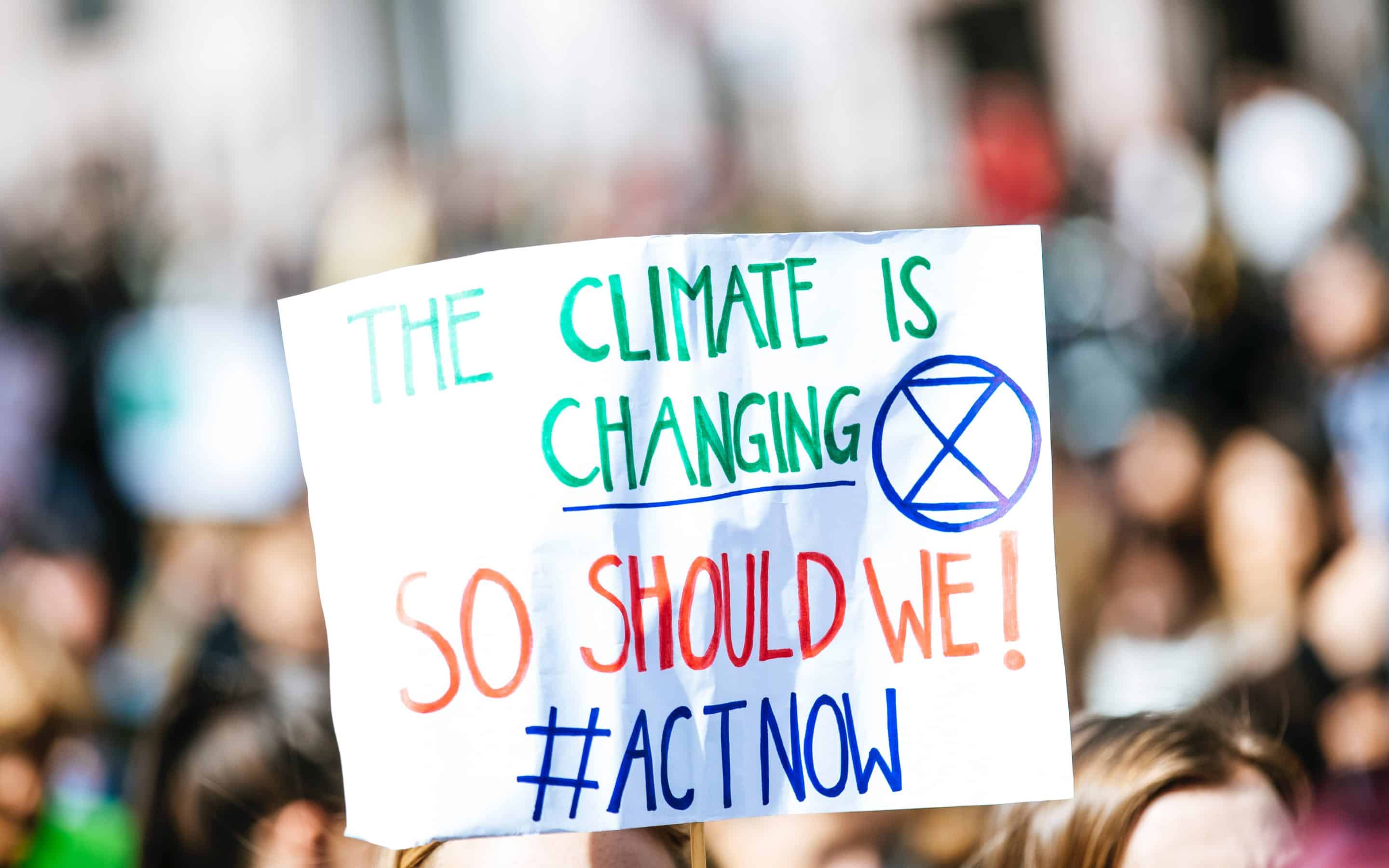 Protest sign reads, "The climate is changing, so should we! #ActNow"