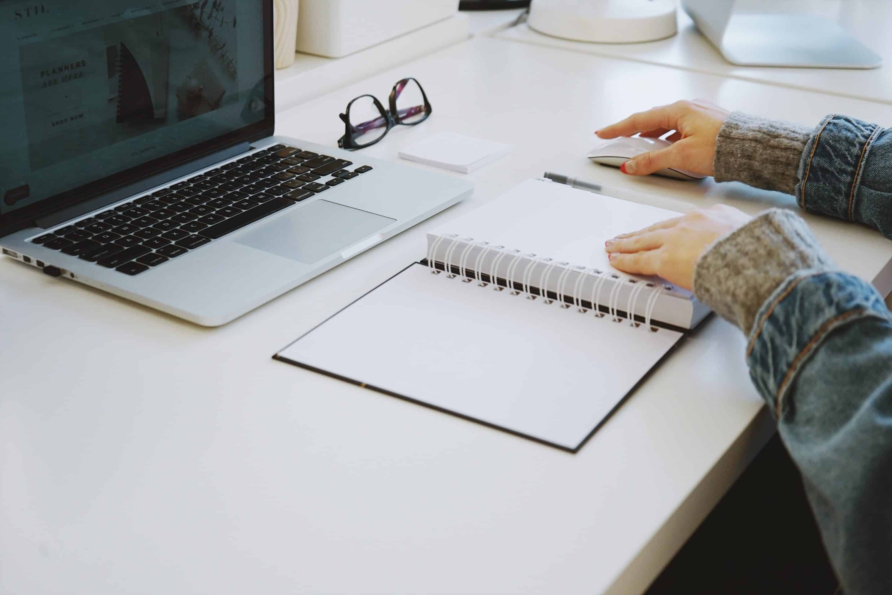 an opened planner lays in front of a laptop